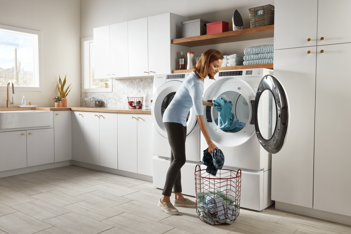 Woman loading laundry into a white washer and dryer